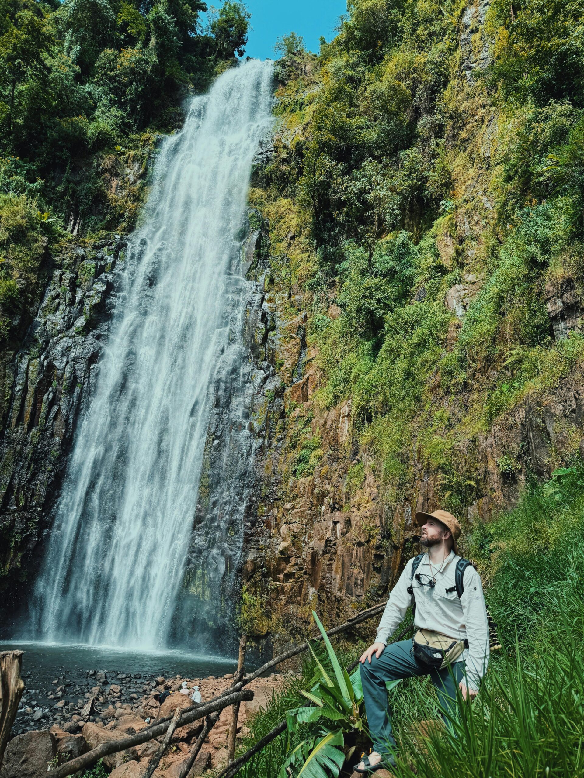 Tourists enjoying Materuni Waterfall surrounded by lush greenery.